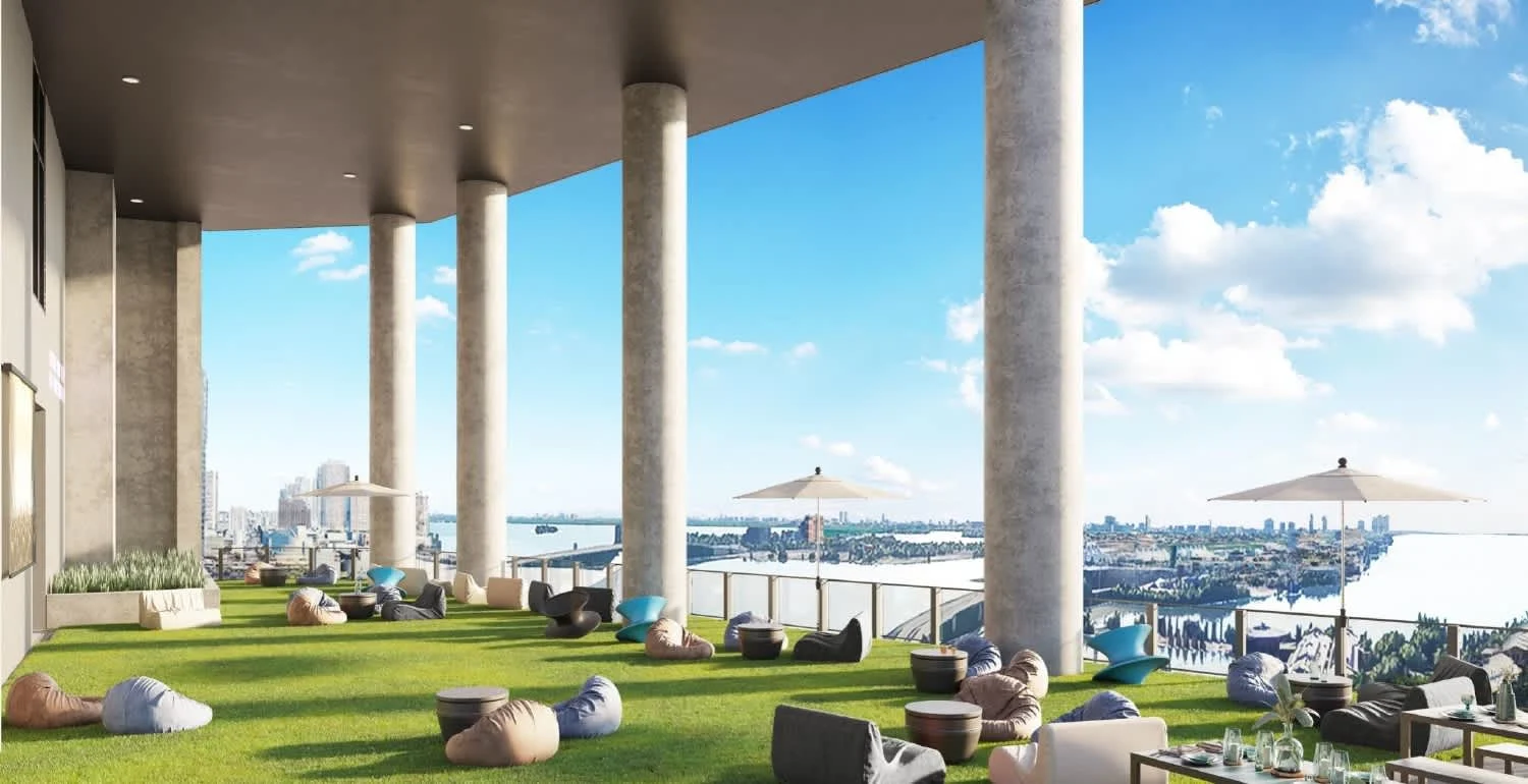 A spacious terrace with green grass, bean bags, and tables, featuring tall columns and a view of the city skyline and water.