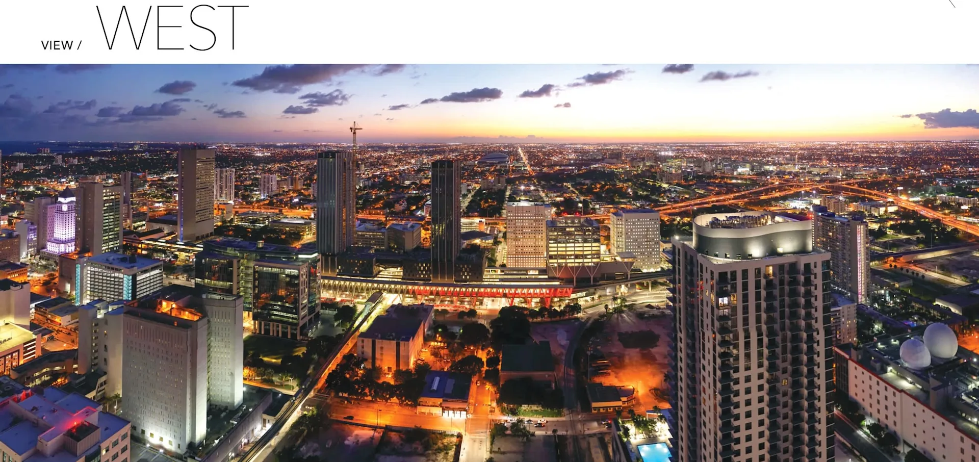 A panoramic view of a city skyline at dusk, showcasing illuminated buildings and streets under a colorful sky.