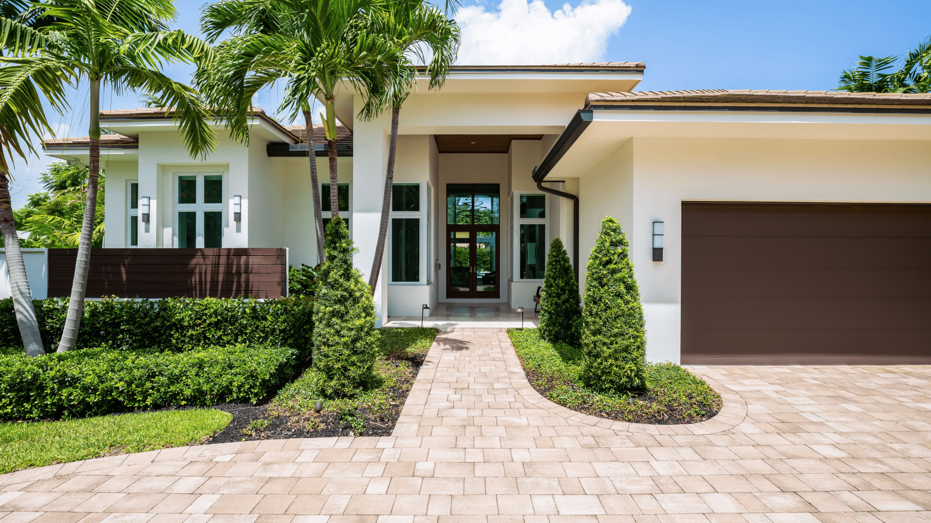 Facade of a beautiful house, with a front garden made up of palms, short grass and tropical plants